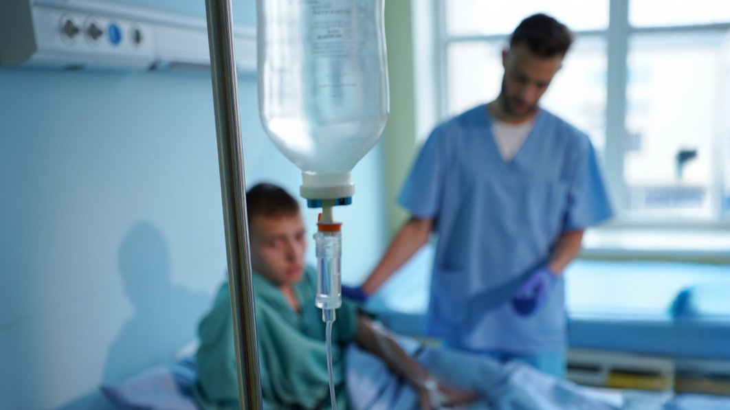 капельница крупным планом, на фоне врач обследует пациента